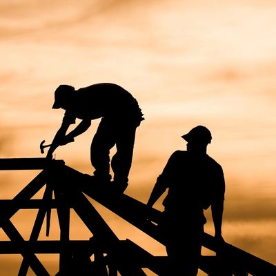 Silhouettes of two construction workers working on a roof during sunset.