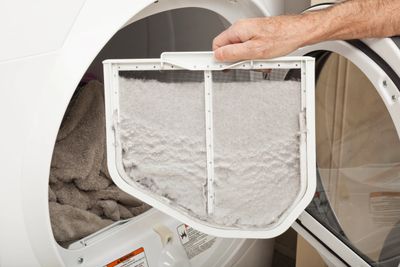 A dryer lint filter with a layer of lint being held in front of a dryer.