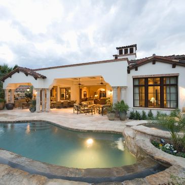 A picture of a home, backyard with a pool with patio furniture and lights on. 