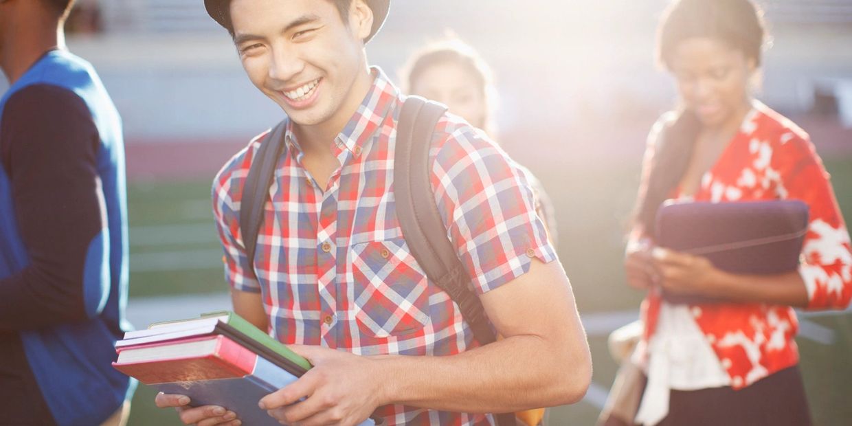 Happy student holding books outdoors with friends in the background.