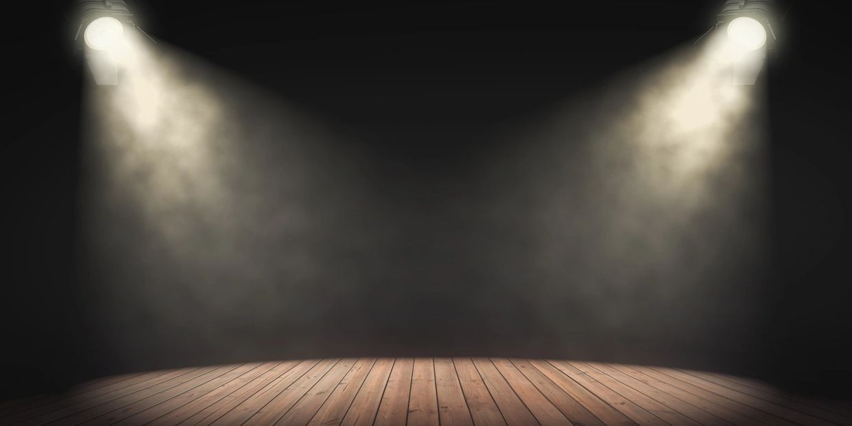 Empty wooden stage illuminated by two spotlights in a dark room.