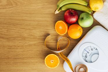 Healthy fruits, measuring tape, and a scale on a wooden surface.