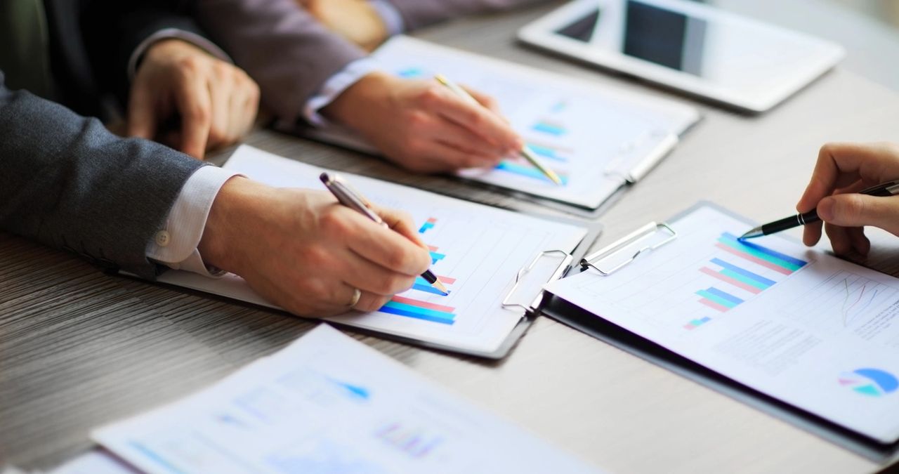 A group of three people review and discuss the same reports on their clipboards.