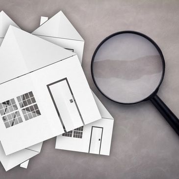 Paper house cutouts beside a magnifying glass on a textured surface.