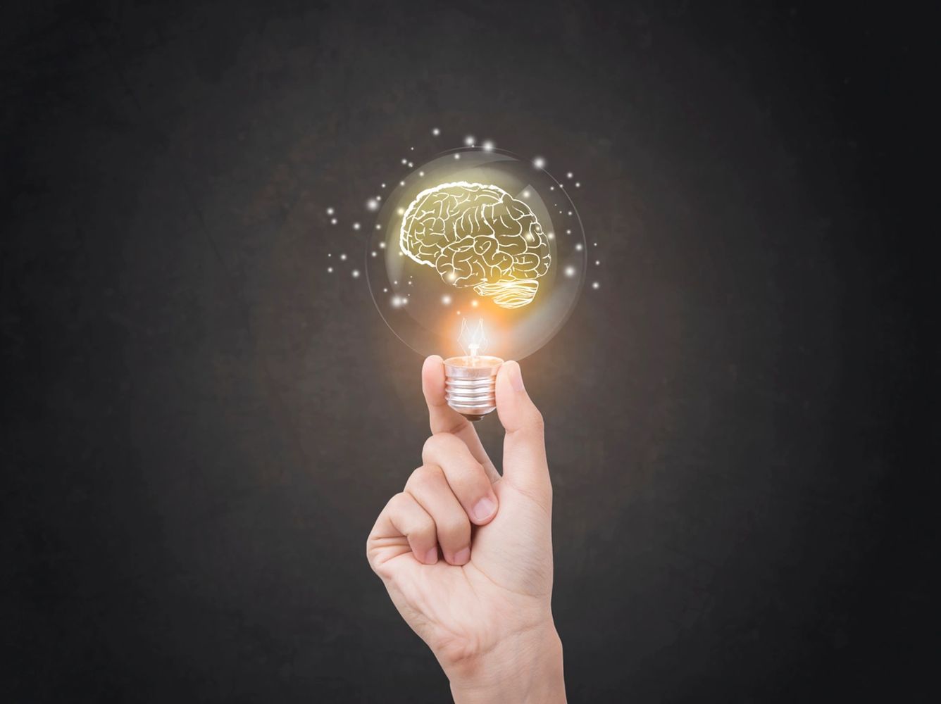 Hand holding a glowing light bulb with a brain illustration inside.