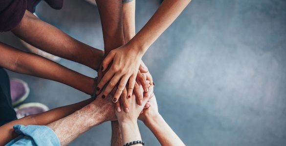 Image of multi-ethnic people standing in a circle with arms extended and hands atop one anothers