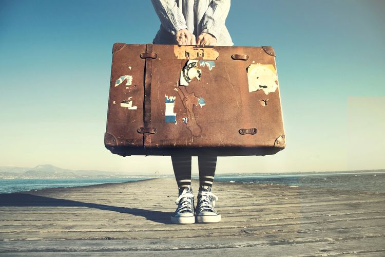 Woman standing on a dock holding suitcase.