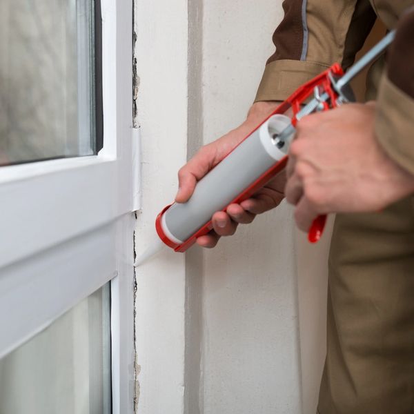 Person applying caulk around a window frame with a caulking gun.