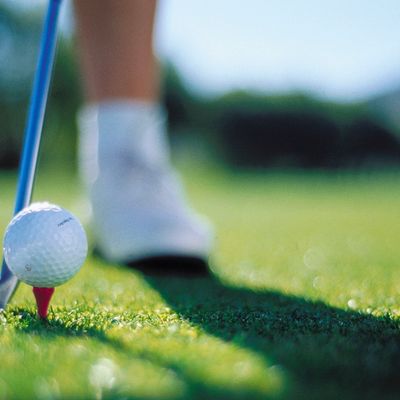 Golf ball on a tee with a player in the background preparing to swing.