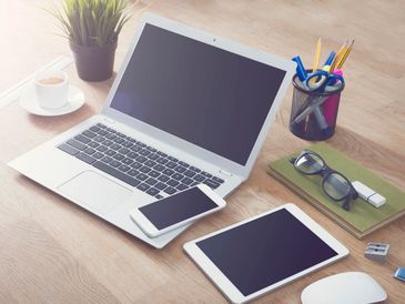 Image of various electronics on a desk (laptop, phone, tablet)