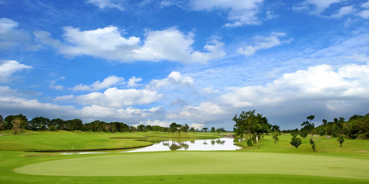 A serene golf course with a water hazard under a partly cloudy blue sky.
