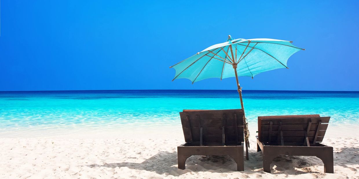 Two wooden lounge chairs with a blue umbrella on a pristine beach.