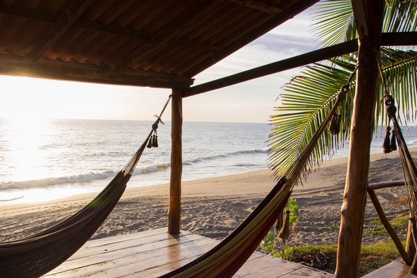 Hammocks on a wooden porch overlooking a tranquil beach at sunset.
