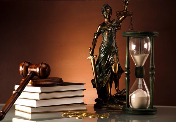 Justice statue, gavel, books, and hourglass symbolize law and time.