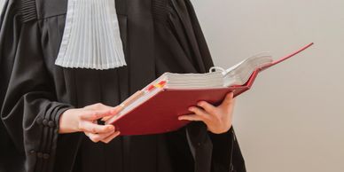 A person in legal robes reading a large red book, likely law-related.