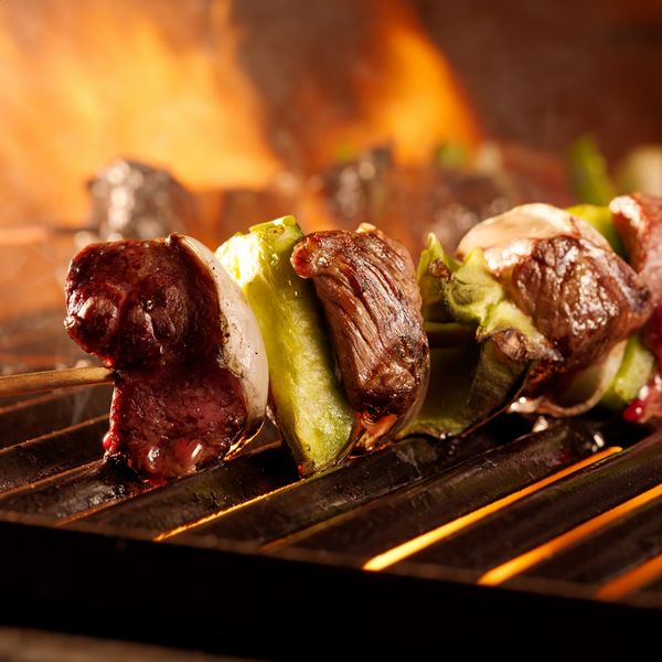 Close-up of meat and vegetables grilling on skewers over flames.