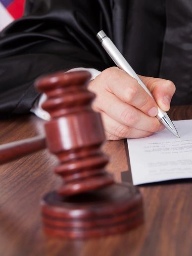 A judge in a black robe signs a legal document with a gavel on the table.