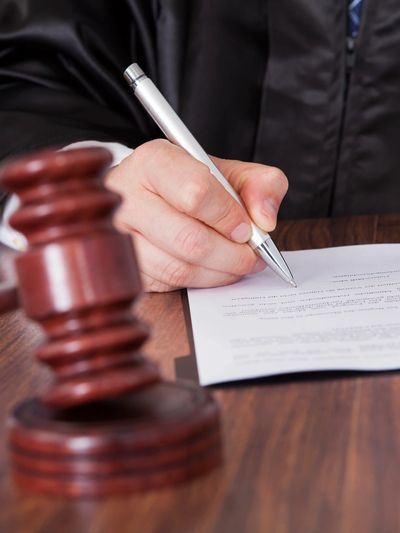 Judge signing a legal document with a gavel on the table.