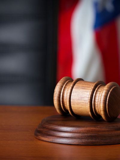 Wooden judge's gavel on desk with blurred American flag background.