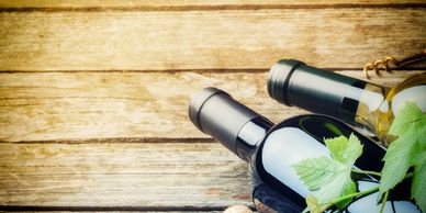Two wine bottles with grape leaves on wooden surface.