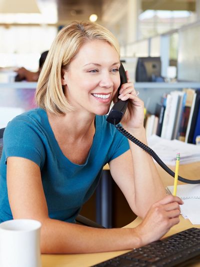 Woman smiling while talking on the phone at her desk.