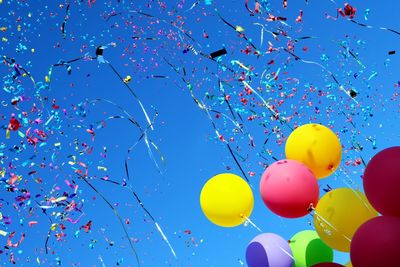 Colorful balloons and confetti against a clear blue sky.