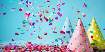 Colorful confetti falling around polka dot and star-patterned party hats.