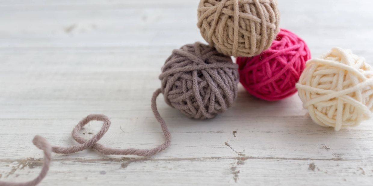 Four balls of yarn in different colors on a wooden surface.