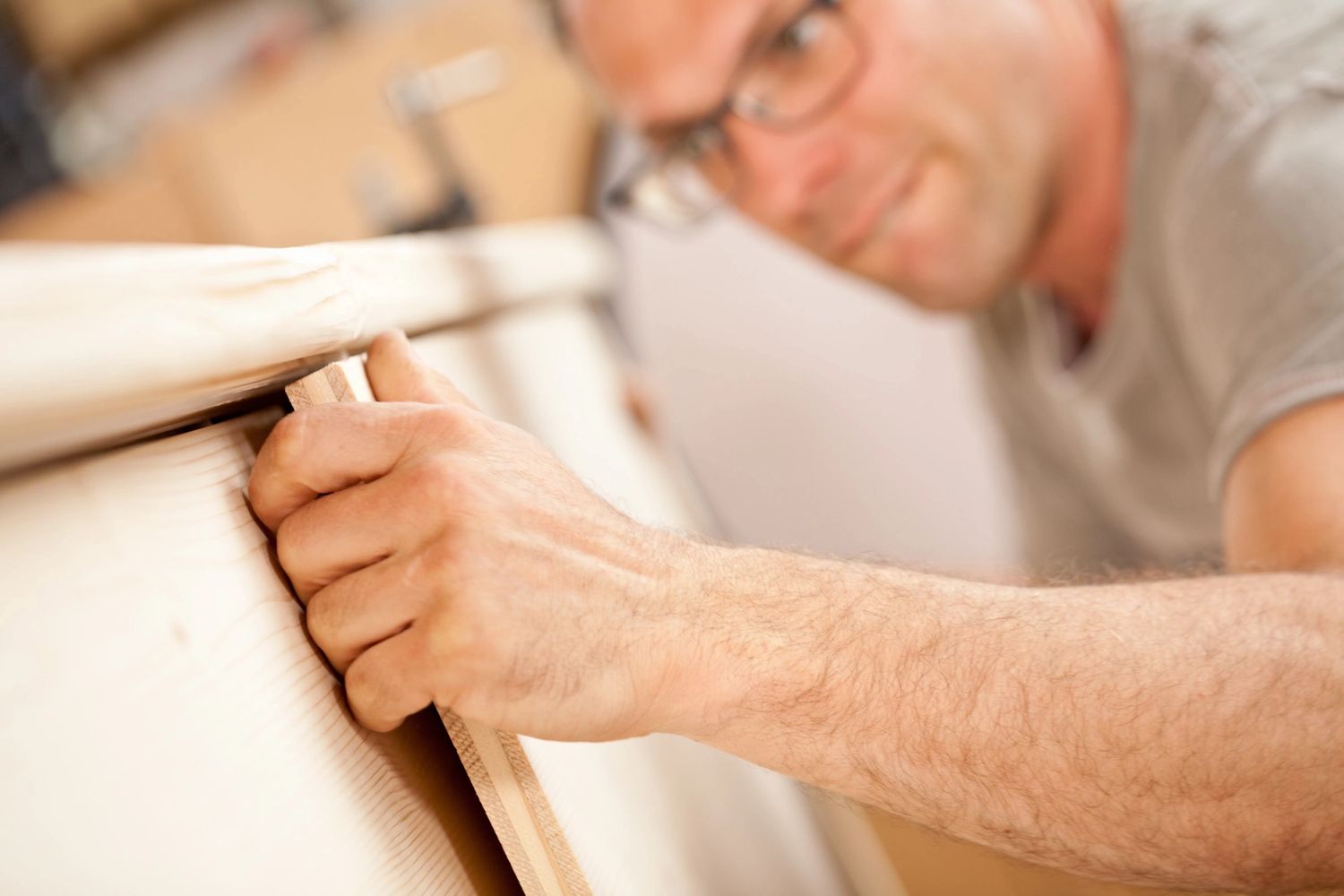 Man sanding a wooden surface with focus on his hand and wood.