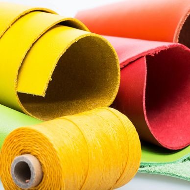 Rolled colorful leather sheets with a spool of yellow thread.