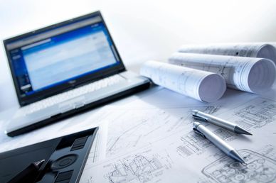 Laptop and technical drawings with pens on a workspace.