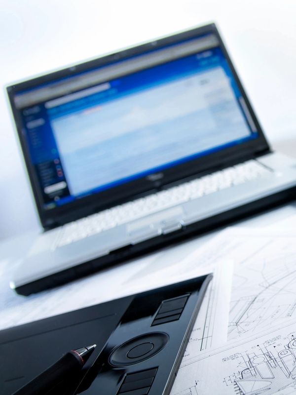 Laptop, rolled architectural blueprints, pens, and drawing tablet on a desk.