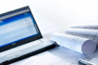 Laptop and rolled-up blueprints on a desk.