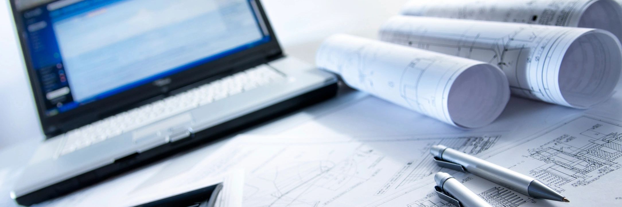 Laptop and architectural plans with pens on a table.