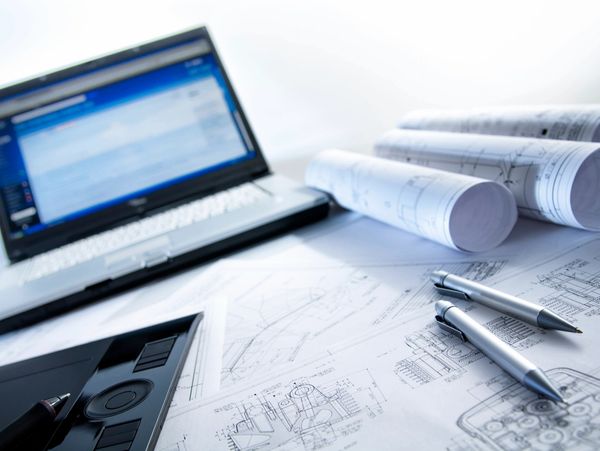 Workspace with laptop, architectural blueprints, pens, and a drawing tablet.