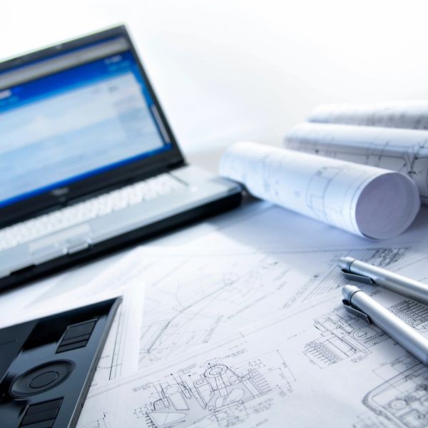 Workspace with laptop, technical drawings, and pens for design work.
