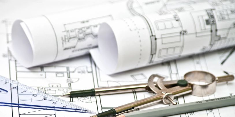 Rolled architectural blueprints with drawing instruments on a desk.