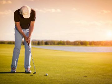 Golfer putting on green during sunset at a golf course.