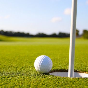 Golf ball resting near the hole on a green golf course under a clear sky.