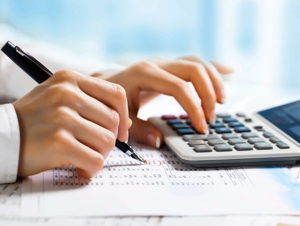 Person using a pen and calculator to work on financial documents.
