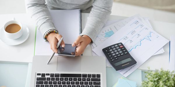 Woman sitting at a desk in front of a laptop while holding a cellular device. 