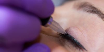 Close-up of eyeliner tattoo being applied on a closed eyelid.