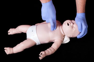 Image shows someone demonstrating CPR using just two fingers on an infant mannequin