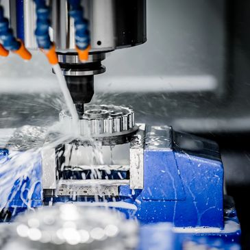 CNC machine cutting a metal gear with coolant spray.