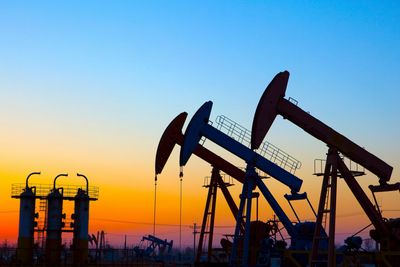 Oil pump jacks silhouetted against a colorful sunset sky.