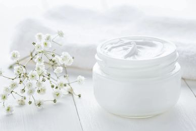 White cream jar with delicate white flowers on a light wooden surface.