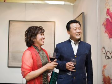 A couple enjoying an art gallery with wine glasses in hand.