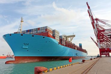 Large blue cargo ship docked with containers stacked on board.