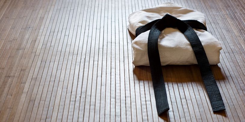Folded martial arts uniform with black belt on wooden floor.
