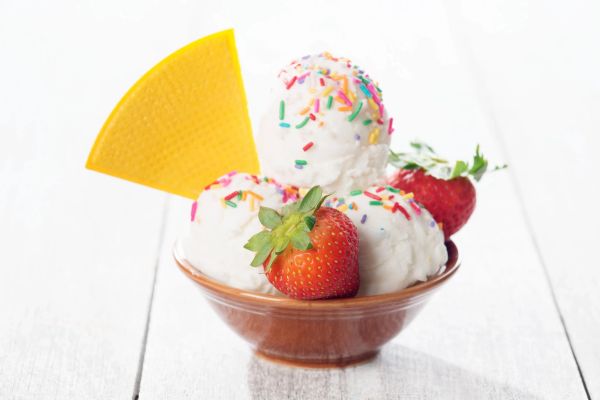 Bowl of vanilla ice cream with sprinkles, strawberries, and a yellow wafer.